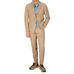 A man wearing a Slowear Light Beige Washed Chinolino Suit with medium-rise trousers, a blue shirt, and colorful sneakers.