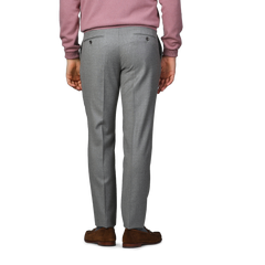 A person wearing Incotex Light Grey Wool Flannel Slim Trousers, a pink sweater, and brown shoes stands facing away.