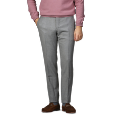 A person wearing a pink sweater, Light Grey Wool Flannel Slim Trousers by Incotex, and brown leather shoes stands with hands in pockets against a plain background.