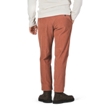 A person in a white long-sleeve shirt and Incotex Muted Orange Cotton Corduroy High Comfort Chinos is standing with one hand in their pocket, showing the back view. They are wearing dark brown shoes.