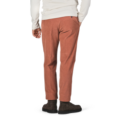 A person in a white long-sleeve shirt and Incotex Muted Orange Cotton Corduroy High Comfort Chinos is standing with one hand in their pocket, showing the back view. They are wearing dark brown shoes.