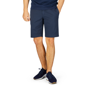 A person wearing Incotex navy blue cotton high comfort shorts and blue sneakers standing with their feet together against a white background.