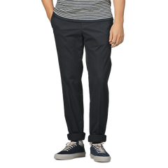 Someone wearing a striped shirt, Incotex Navy Blue Cotton Royal Batavia Regular Chinos, and dark sneakers stands with one hand in their pocket.