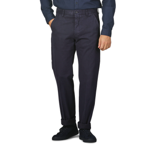 A person stands against a plain background, hands in pockets, dressed in a dark blue shirt paired with Incotex's Navy Blue Cotton Stretch Model 8 Chinos.