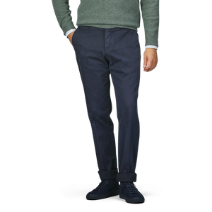 A person wearing Incotex's navy blue cotton twill regular chinos, a green sweater, and black shoes stands with one hand in their pocket.