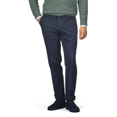 A person wearing Incotex's navy blue cotton twill regular chinos, a green sweater, and black shoes stands with one hand in their pocket.