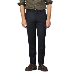 A man dressed in Incotex Navy Blue Wool Flannel Slim Trousers, a brown shirt, and brown shoes stands with his arms by his sides against a plain background. The slim fit of the trousers highlights his relaxed yet refined stance.