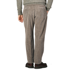 A person stands facing away, wearing Incotex stone grey cotton corduroy regular fit trousers paired with a grey sweater and dark shoes.