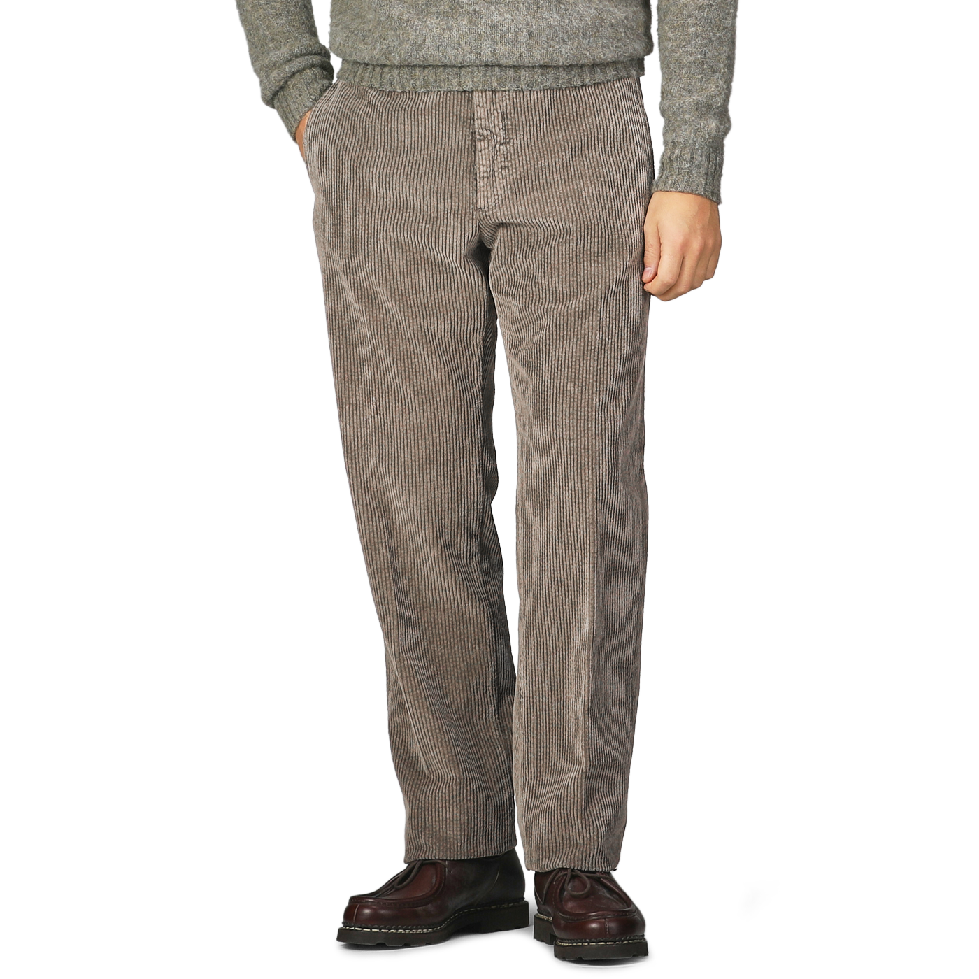 A person in Incotex's Stone Grey Cotton Corduroy Regular Fit Trousers and brown shoes, paired with a gray sweater, stands with hands in pockets against a plain background.