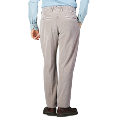 A person wearing taupe beige cotton corduroy regular fit trousers from Incotex, a light blue shirt, and brown shoes is standing with a casual stance, facing away from the camera.