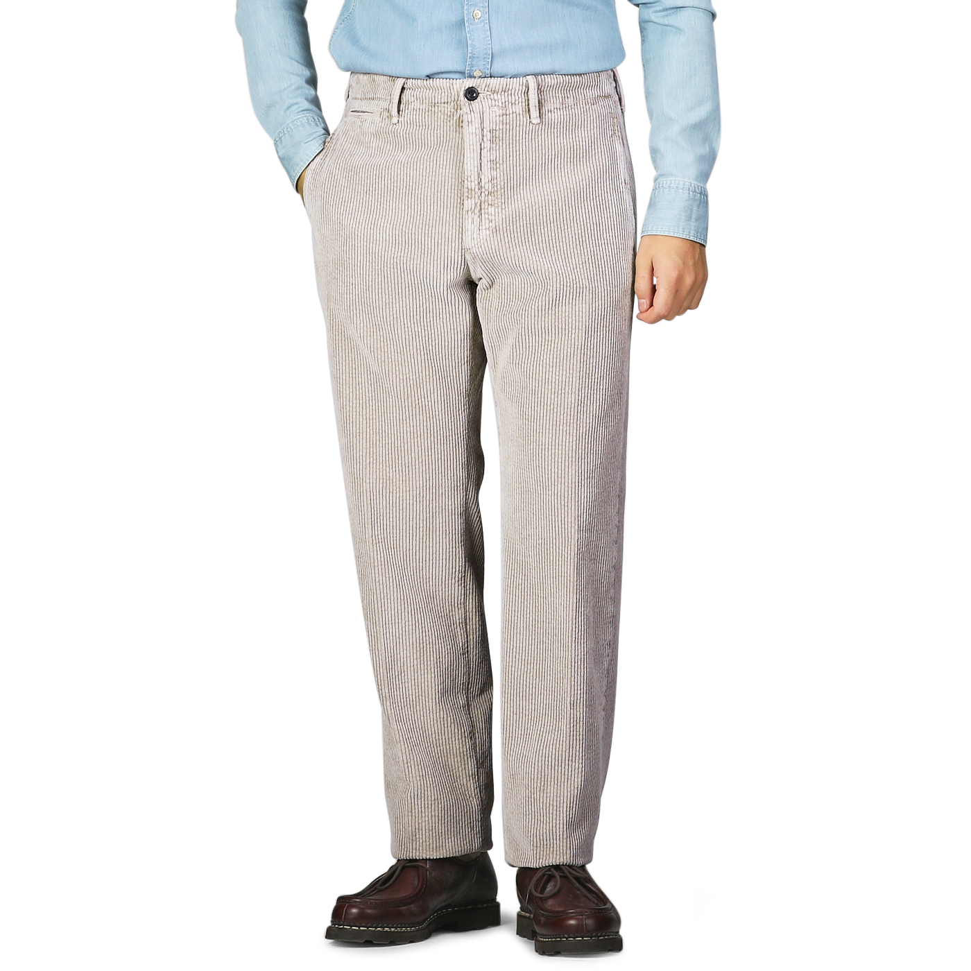 A person stands wearing Incotex taupe beige cotton corduroy regular fit trousers, a light blue denim shirt, and brown shoes, with their hands in their pockets.