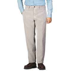 A person stands wearing Incotex taupe beige cotton corduroy regular fit trousers, a light blue denim shirt, and brown shoes, with their hands in their pockets.