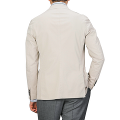 An individual wearing an Incotex Taupe Beige Washed Cotton Batavia Blazer in slim fit and gray pants is seen with their back turned against a neutral background.