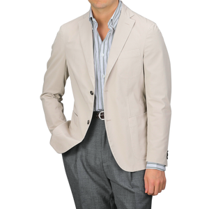 A man wears an Incotex Taupe Beige Washed Cotton Batavia Blazer over a striped shirt and gray trousers, shown from shoulders to waist. The unstructured blazer offers a relaxed yet polished style, showcasing the ensemble's versatility and modern appeal.