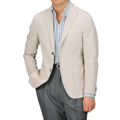 A man wears an Incotex Taupe Beige Washed Cotton Batavia Blazer over a striped shirt and gray trousers, shown from shoulders to waist. The unstructured blazer offers a relaxed yet polished style, showcasing the ensemble's versatility and modern appeal.