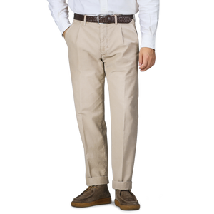 A person wearing Incotex Washed Beige Single Pleat Cotton Slacks, a white shirt, a brown belt, and brown shoes stands with hands in pockets.