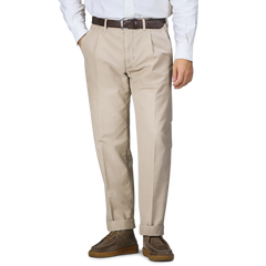 A person wearing Incotex Washed Beige Single Pleat Cotton Slacks, a white shirt, a brown belt, and brown shoes stands with hands in pockets.