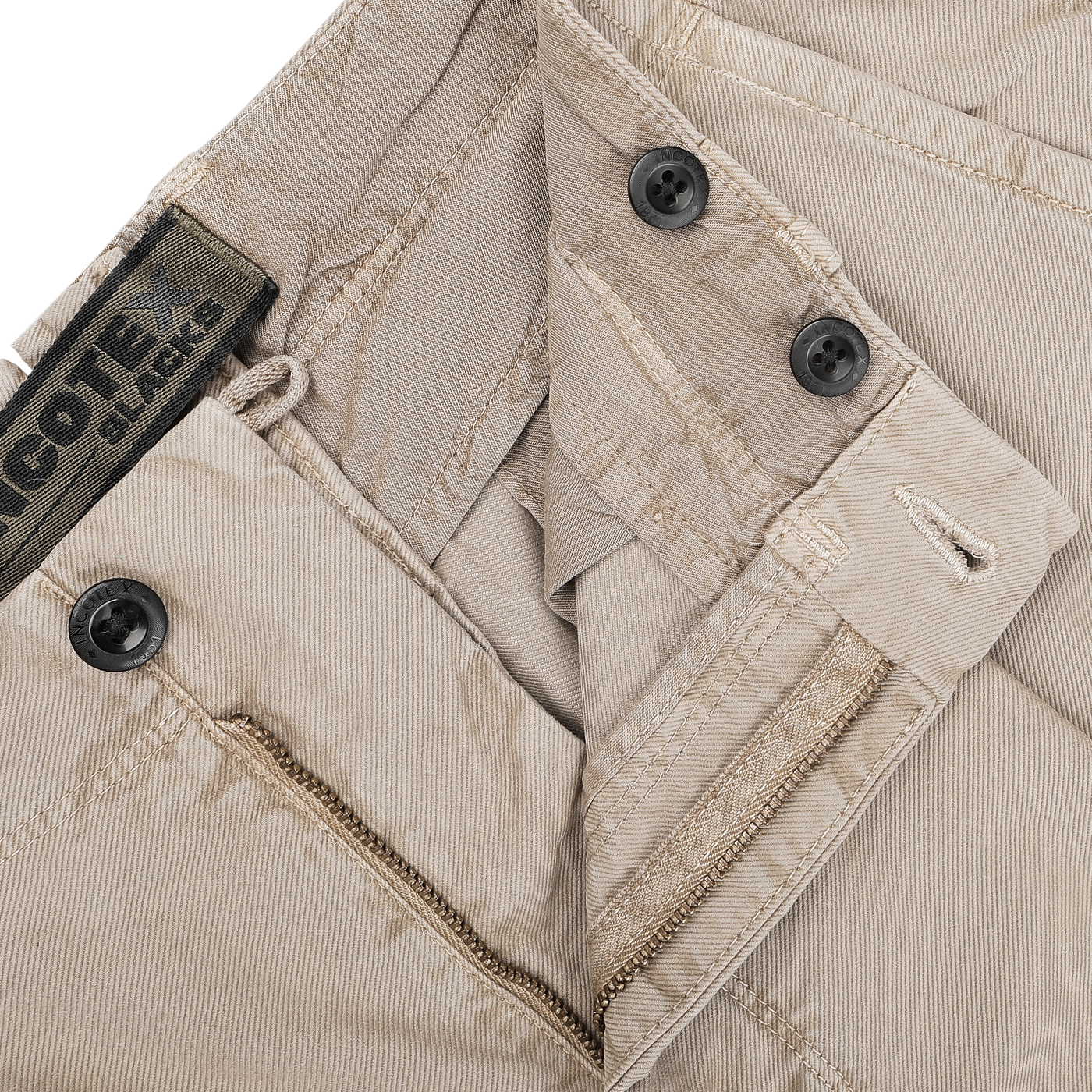 A close-up of the Washed Beige Single Pleat Cotton Slacks by Incotex, highlighting their black buttons and visible zipper. A tag reads "COTE AUCTIONS.