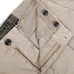 A close-up of the Washed Beige Single Pleat Cotton Slacks by Incotex, highlighting their black buttons and visible zipper. A tag reads "COTE AUCTIONS.