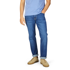 Man wearing Jeanerica Medium Blue Washed Cotton TM005 jeans and light blue t-shirt with tan shoes, standing with his left hand in pocket.