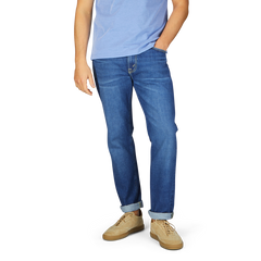 Man wearing Jeanerica Medium Blue Washed Cotton TM005 jeans and light blue t-shirt with tan shoes, standing with his left hand in pocket.