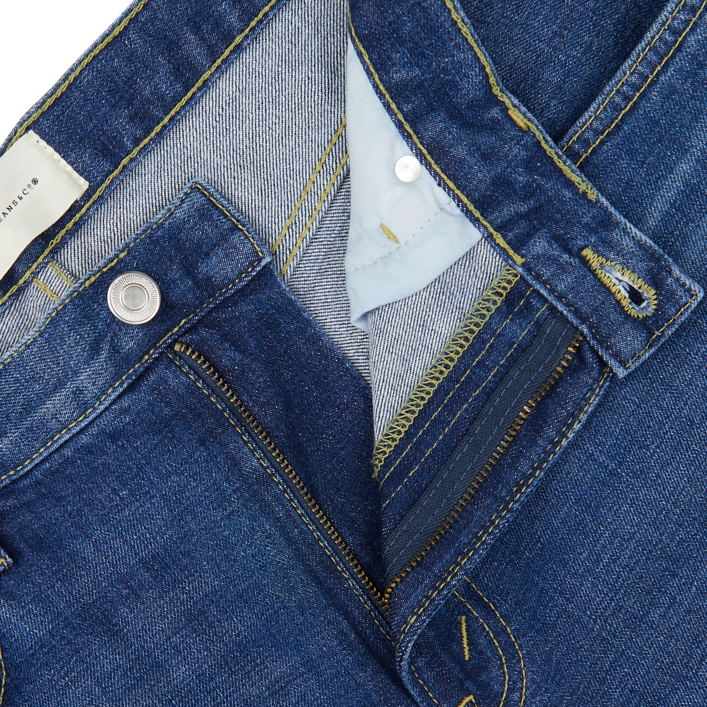 Close-up of a blue Jeanerica denim jacket with detailed stitching and a light blue shirt collar underneath, featuring the Medium Blue Washed Cotton TM005 Jeans.