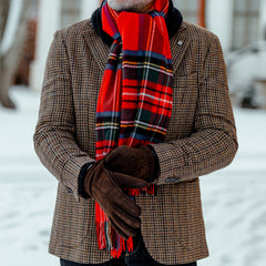 A person wearing a Red Checked Royal Stewart Cashmere Scarf by Johnstons Of Elgin, a brown checkered coat, and gloves stands in a snowy outdoor setting.