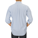 Person wearing a light blue, long-sleeved Kamakura Shirts' Blue Striped Washed Cotton Oxford BD Shirt, seen from the back facing a neutral background.