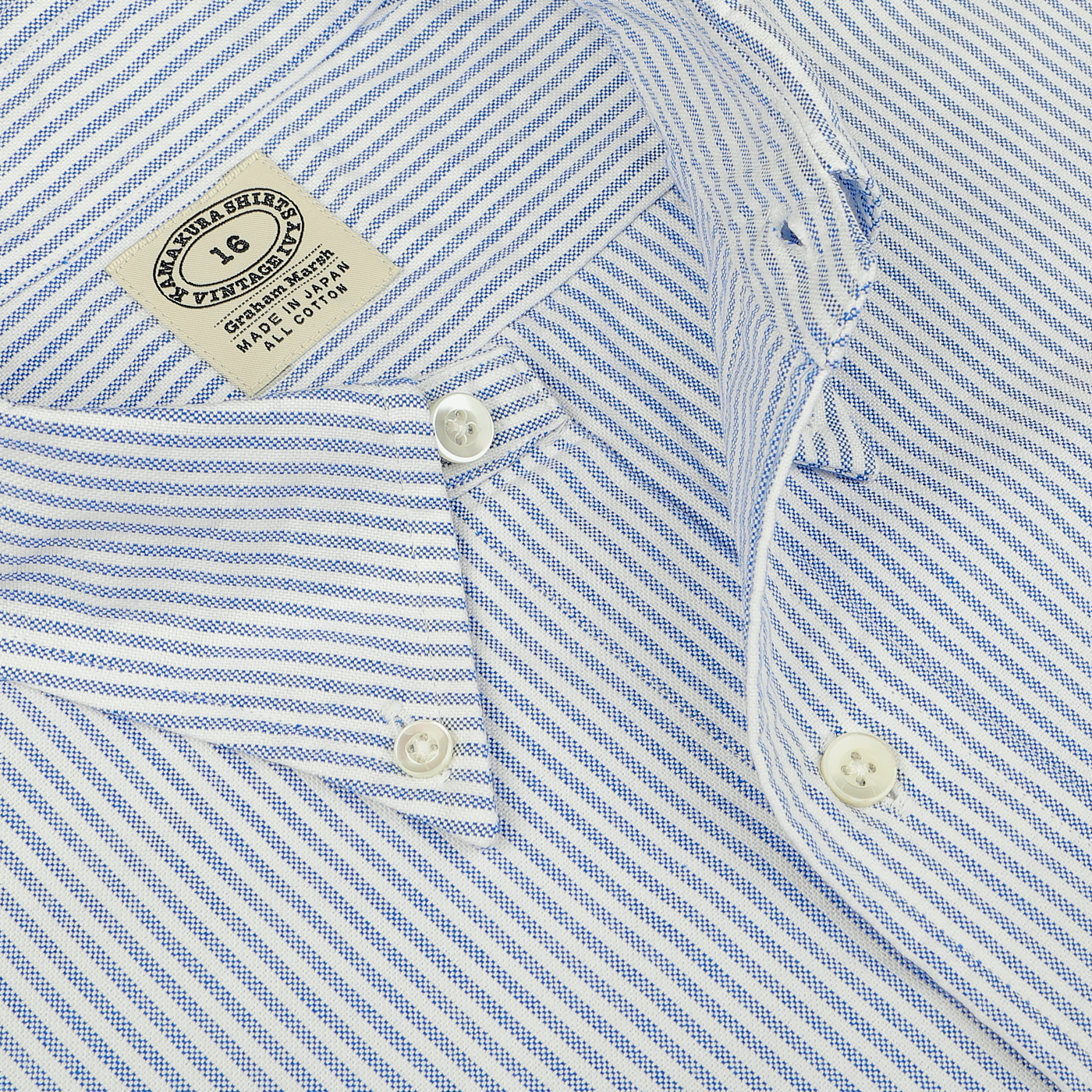 Close-up of a blue and white striped button-down shirt from Kamakura Shirts, displays its label with washing instructions and size "16." This pure cotton oxford shirt, named the Blue Striped Washed Cotton Oxford BD Shirt, features a classic three-inch button-down collar.