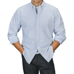 Person wearing a Kamakura Shirts Blue Striped Washed Cotton Oxford BD Shirt over a white t-shirt, with hands in the pockets of dark jeans against a gray background.