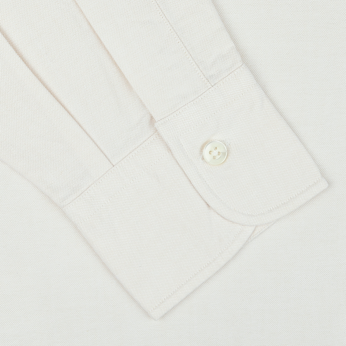 Close-up of the cuff from an Ecru Washed Cotton Oxford BD Shirt by Kamakura Shirts. The casual shirt from the Vintage Ivy collection features a single white button fastened on its subtly textured pure cotton oxford fabric.