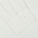 Close-up of the cuff from an Ecru Washed Cotton Oxford BD Shirt by Kamakura Shirts. The casual shirt from the Vintage Ivy collection features a single white button fastened on its subtly textured pure cotton oxford fabric.