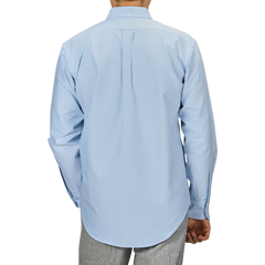 A man is seen from the back wearing a light blue Kamakura Shirts' Washed Cotton Oxford BD Shirt paired with grey trousers, set against a plain background.