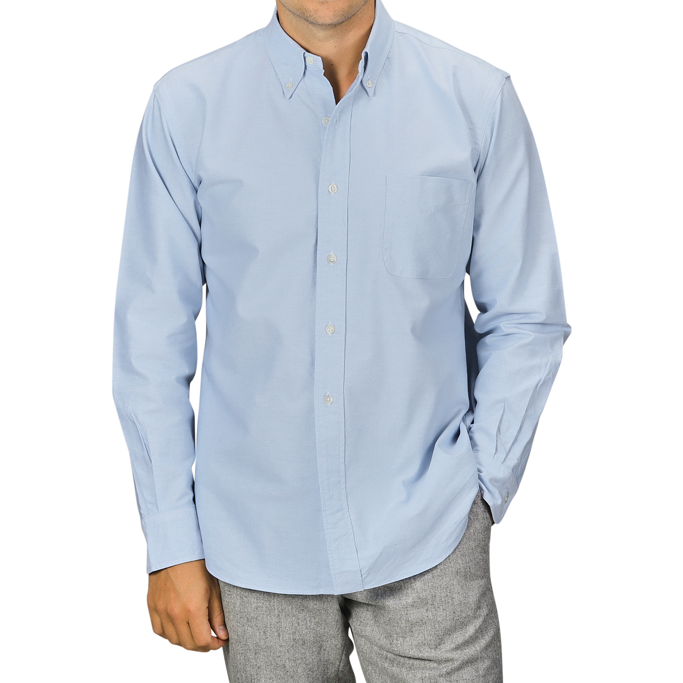 A man wearing a Light Blue Washed Cotton Oxford BD Shirt from Kamakura Shirts and gray trousers. The pure cotton oxford shirt has a chest pocket, and the man has his hands in his pockets.