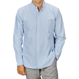 A man wearing a Light Blue Washed Cotton Oxford BD Shirt from Kamakura Shirts and gray trousers. The pure cotton oxford shirt has a chest pocket, and the man has his hands in his pockets.