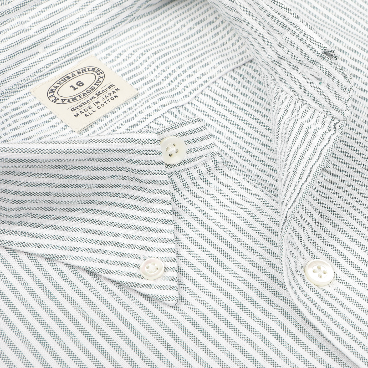 Close-up of the Green Striped Washed Cotton Oxford BD Shirt by Kamakura Shirts, showcasing its button-down collar. The size label reads "16," and the brand label is clearly visible. Made from pure cotton oxford, the fabric features a light base with dark green stripes.