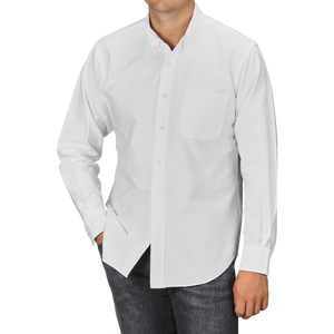 A person is wearing a White Washed Cotton Oxford BD Shirt from Kamakura Shirts, featuring a long-sleeve button-up design with a chest pocket, paired with dark jeans and their left hand in the pocket.