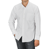 A person is wearing a White Washed Cotton Oxford BD Shirt from Kamakura Shirts, featuring a long-sleeve button-up design with a chest pocket, paired with dark jeans and their left hand in the pocket.