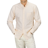 A person wearing a Yellow Striped Washed Cotton Oxford BD Shirt from Kamakura Shirts, paired with white pants, standing with hands in pockets.