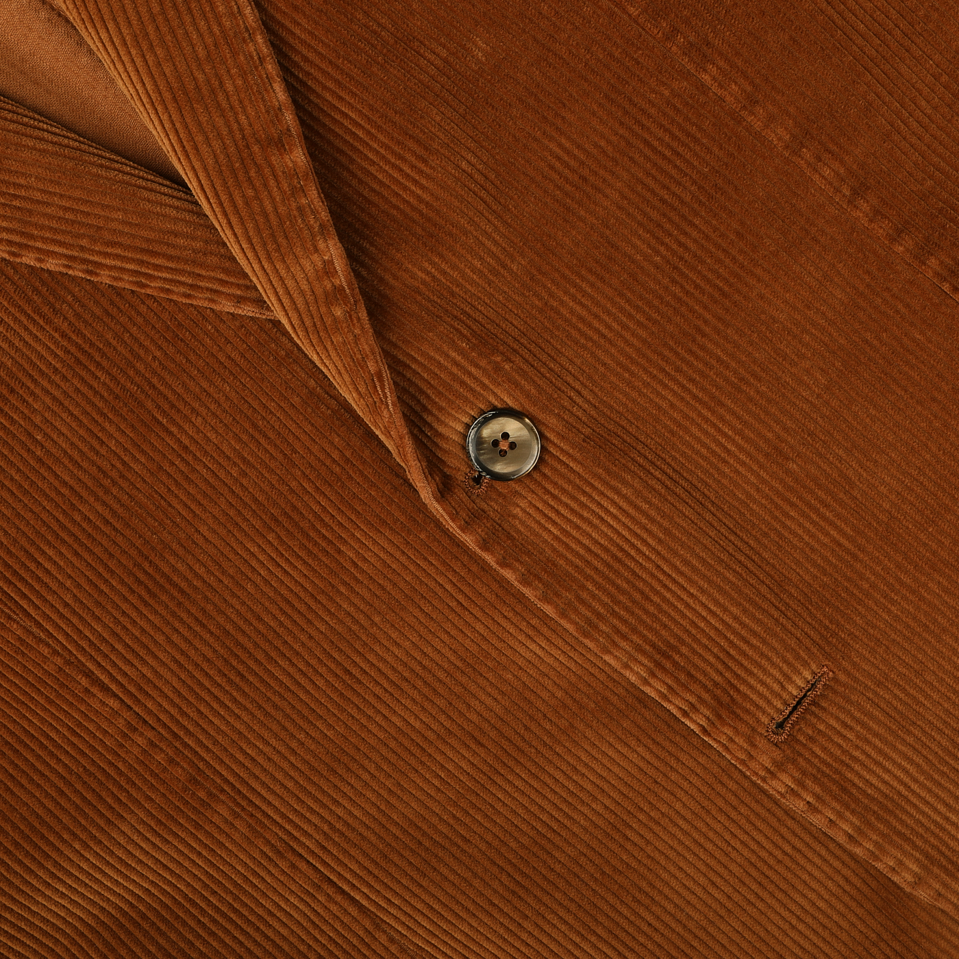 A close-up of the L.B.M. 1911 Cinnamon Brown Cotton Corduroy Blazer reveals a single button fastened through a buttonhole. The pure cotton corduroy fabric showcases its characteristic ridged texture, offering both style and comfort.