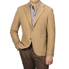 A person wearing the L.B.M. 1911 Camel Beige Brushed Wool Slim Blazer over a striped shirt and brown pants stands with one hand in their pocket, exuding an effortlessly sophisticated style.