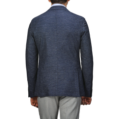 Rear view of a person in an L.B.M. 1911 Dark Blue Linen Cotton Jersey Blazer and light gray pants, set against a plain gray background.