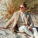 Modified Description: A man sitting on the sand in a Light Beige Cotton Corduroy Blazer by L.B.M. 1911 and white pants.