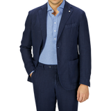 Man in a slim fit L.B.M. 1911 navy blue washed linen suit over a light blue shirt, standing against a grey background. Only the torso and arms are visible.