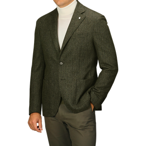 Man wearing an L.B.M. 1911 Dark Green Wool Cashmere Herringbone Blazer over a white turtleneck sweater, paired with matching dark green slim fit pants, standing with his left hand in his pocket. His face is not visible.