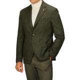 Man wearing an L.B.M. 1911 Dark Green Wool Cashmere Herringbone Blazer over a white turtleneck sweater, paired with matching dark green slim fit pants, standing with his left hand in his pocket. His face is not visible.