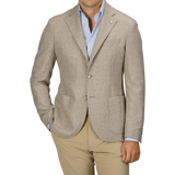 A man wearing an Oatmel Beige Shetland Wool Cashmere Blazer by L.B.M. 1911, paired with a light blue dress shirt and beige pants, stands with his hands in his pockets. The slim fit, seasonal blazer features two buttons and patch pockets.