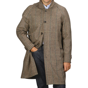 A person stands wearing a L'Impermeabile Beige Houndstooth Wool Tweed Reversible Coat with their right hand in their jeans pocket.