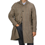 A person stands wearing a L'Impermeabile Beige Houndstooth Wool Tweed Reversible Coat with their right hand in their jeans pocket.