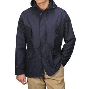 A person wearing L'Impermeabile's Navy Blue Waxed Cotton Bob Short Parka and beige pants keeps their face hidden with a water-repellant jacket featuring buttoned pockets and a front closure.